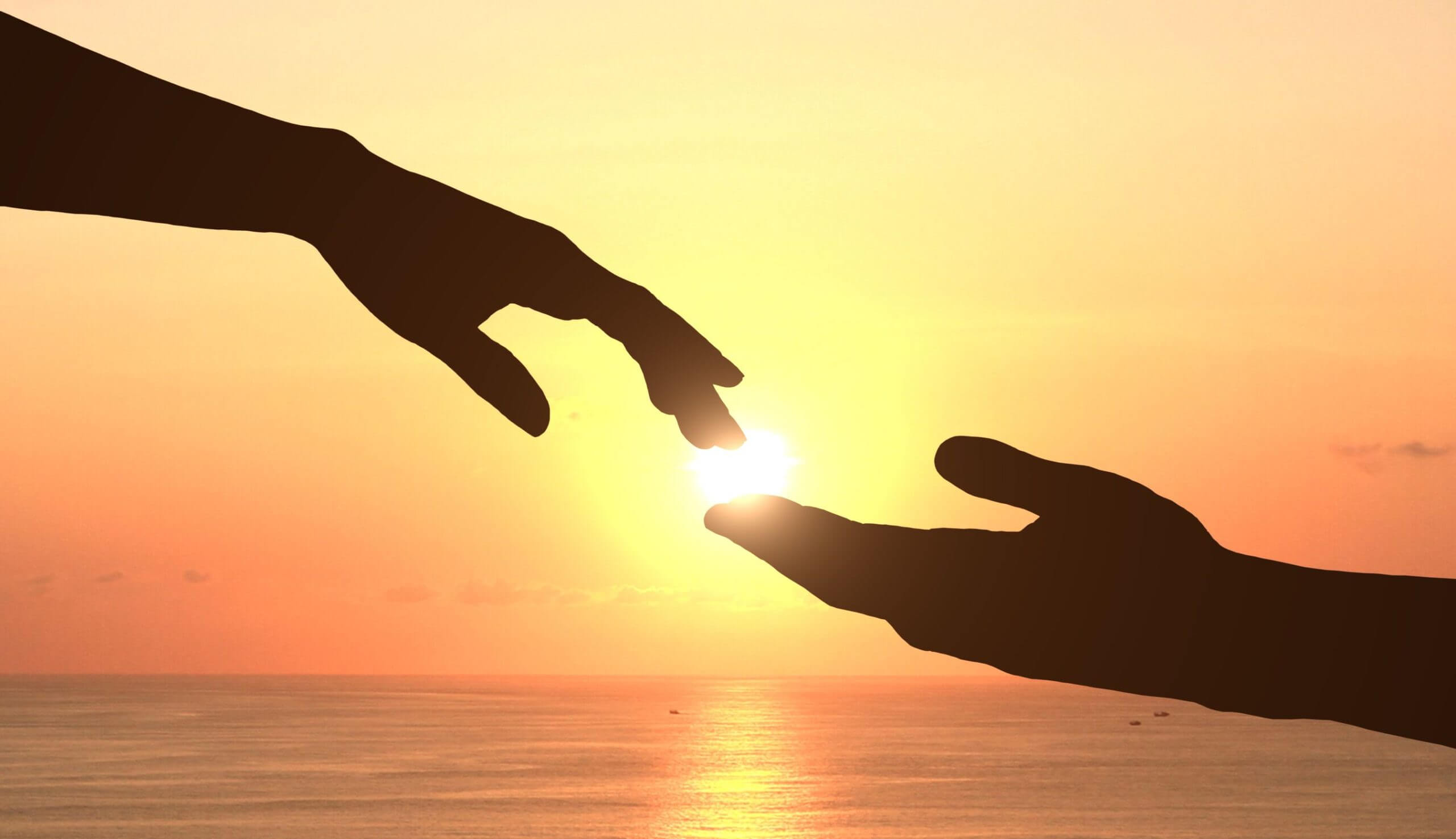 Deux mains qui se rejoignent devant un coucher de soleil au bord de mer